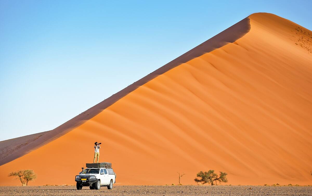 Mann steht auf einem Jeep und macht Fotos in der Wüste